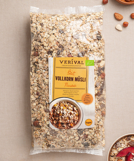 Eine Grpßpackung Nuss-Vollkorn-Müsli von Verival Bio liegt auf einer hellen Unterlage, umgeben von verstreuten Nüssen und Haferflocken und bietet ein leckeres, ballaststoffreiches, veganes Frühstück für deinen Tag.