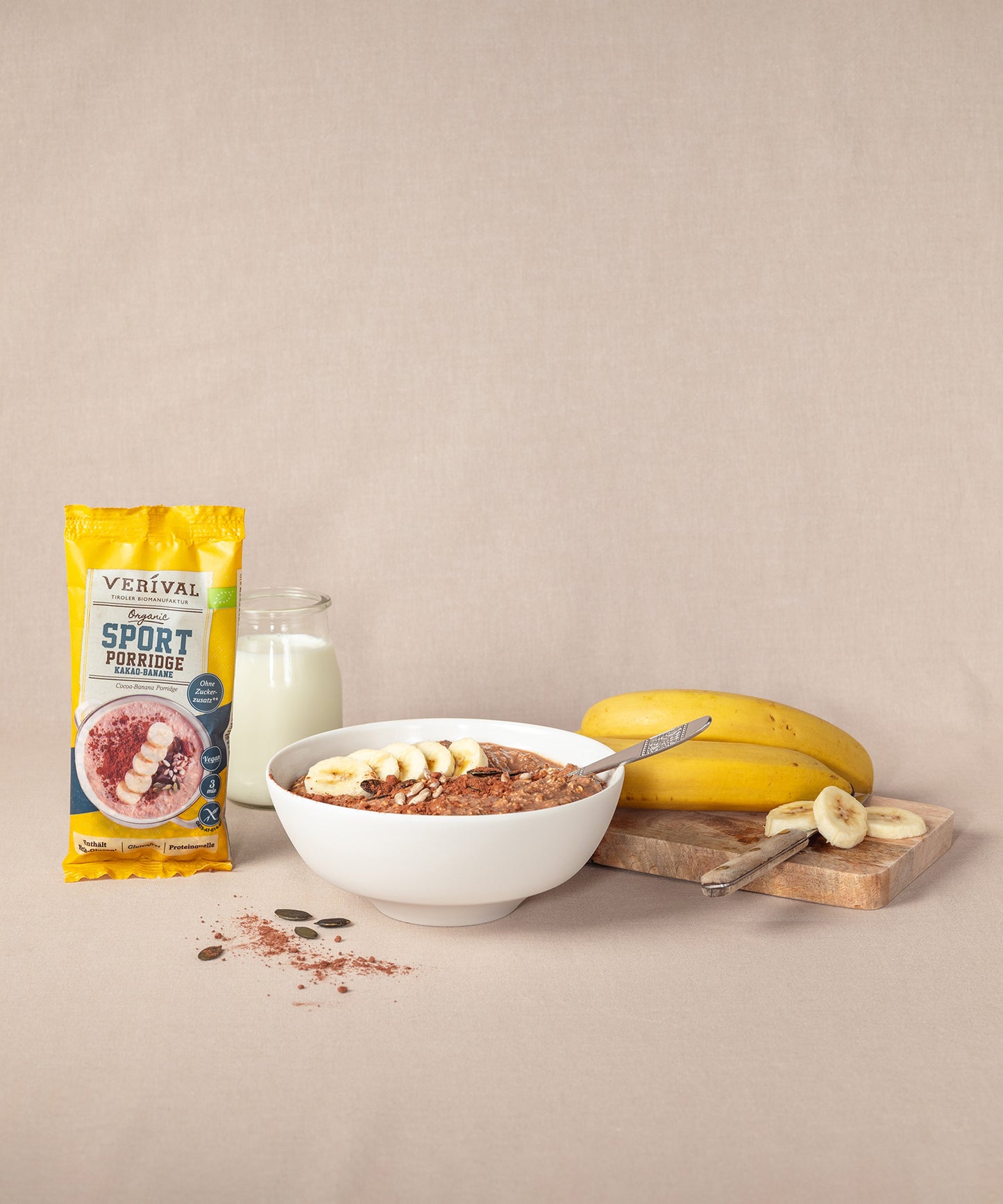 Das Verival „Breakfast Lover“-Set besteht aus Protein Frühstück Sport Porridge und einer eleganten Porzellan-Schüssel. Daneben ist ein Glas Milch und ein Schneidebrett mit Bananen zu sehen.