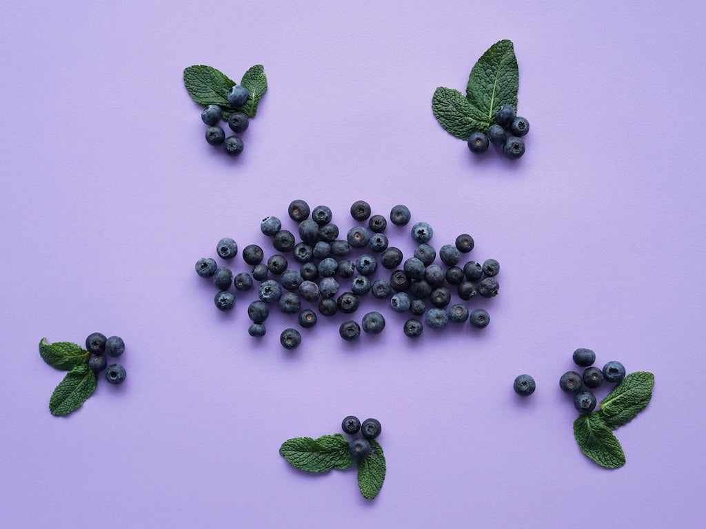 Heidelbeeren und Minzblätter sind auf einer violetten Oberfläche angeordnet.