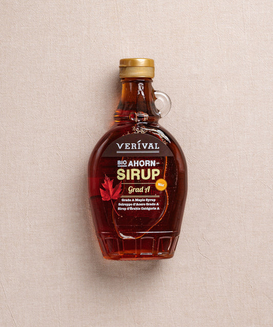 Eine Flasche Ahornsirup Grad A der Verival Bio GmbH steht auf einem beigen Hintergrund, mit einem roten Ahornblatt und mehrsprachigen Produktdetails versehen, die die Herkunft aus der Frühjahrs-Ernte hervorheben.